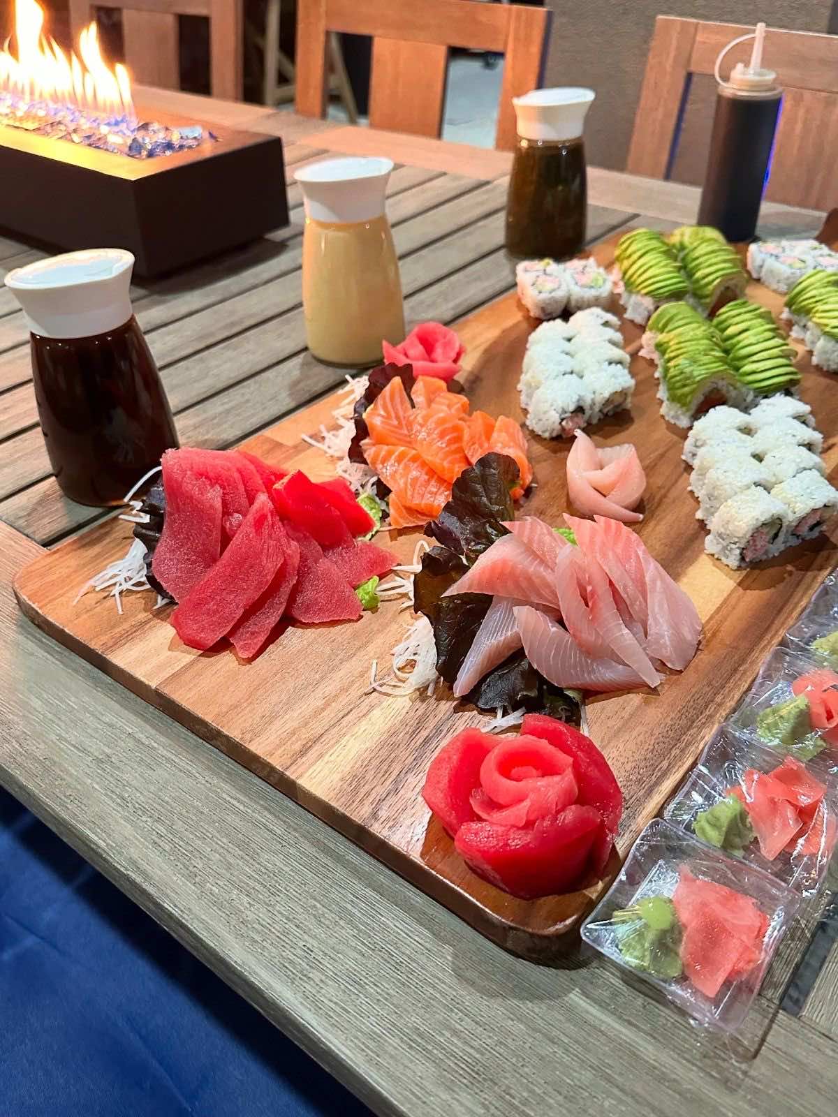 A sushi and sashimi board on the table beside a lit fire pit