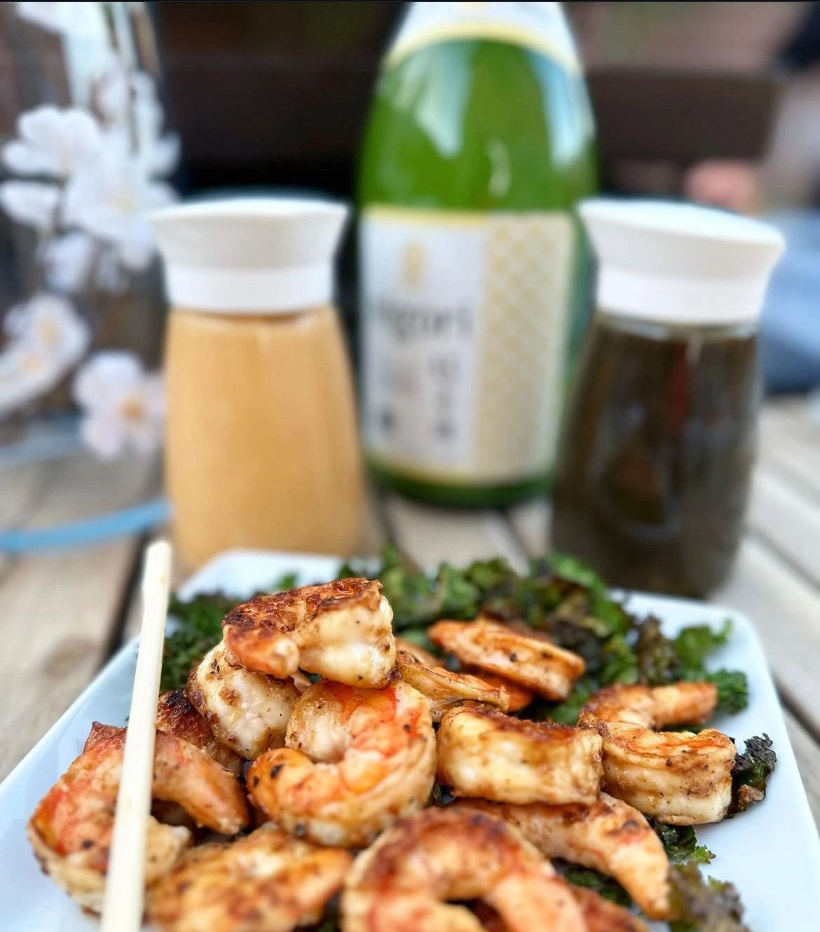 Hibachi shrimp piled over crispy kale, Chef Koma's sauce bottles behind